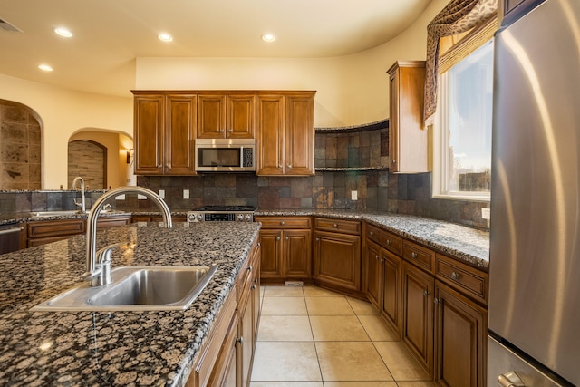 kitchen featuring tasteful backsplash, arched walkways, appliances with stainless steel finishes, a sink, and light tile patterned flooring