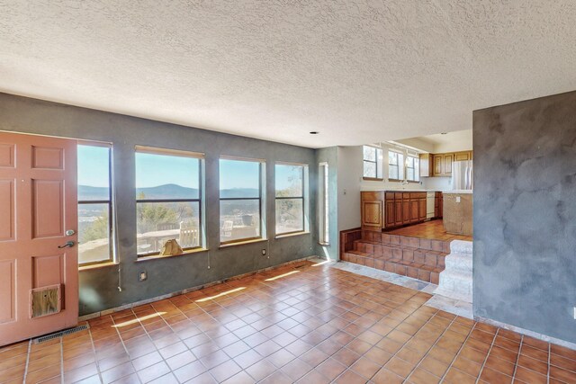 unfurnished living room with tile patterned flooring, a sink, baseboards, visible vents, and a textured ceiling