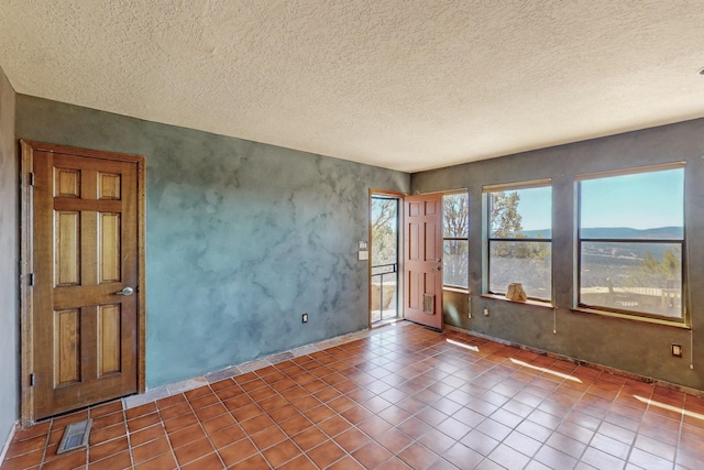 spare room featuring baseboards, visible vents, a textured ceiling, and tile patterned flooring