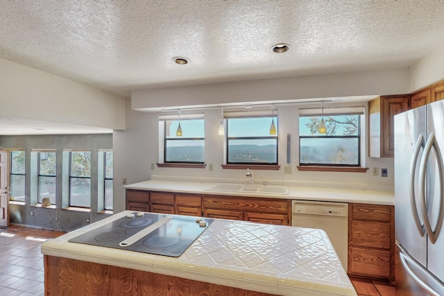 kitchen featuring a textured ceiling, black electric stovetop, a sink, freestanding refrigerator, and brown cabinetry