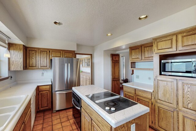 kitchen with a textured ceiling, a sink, tile counters, stainless steel appliances, and a center island