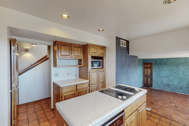 kitchen with a textured ceiling, stainless steel microwave, light tile patterned floors, electric cooktop, and tile countertops