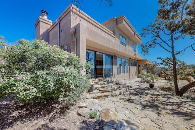 rear view of house with a chimney, stucco siding, and a patio area