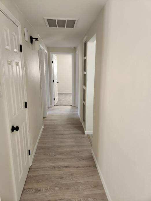 hall with baseboards, light wood-type flooring, and visible vents