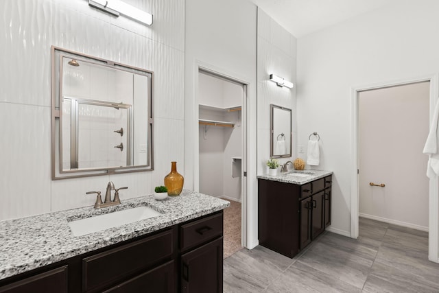 bathroom with a walk in closet, tiled shower, two vanities, and a sink