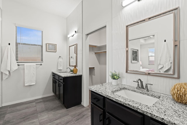 bathroom with baseboards, a sink, and two vanities