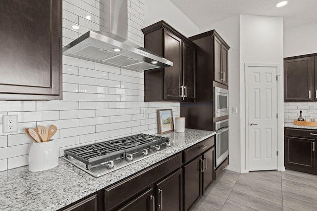 kitchen featuring light stone countertops, appliances with stainless steel finishes, wall chimney exhaust hood, and tasteful backsplash