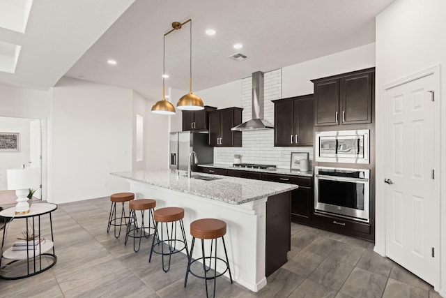 kitchen featuring visible vents, a breakfast bar, wall chimney exhaust hood, a sink, and stainless steel appliances