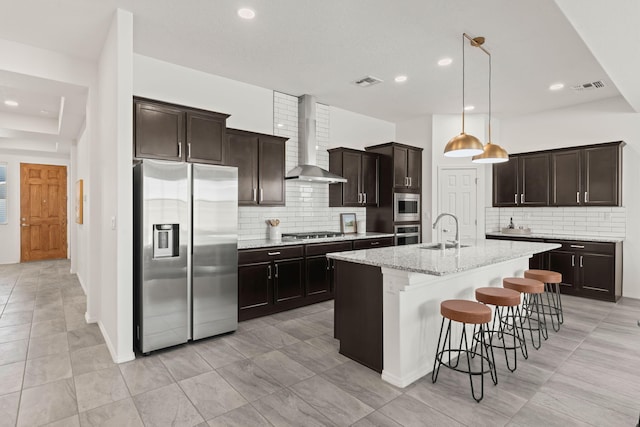kitchen with wall chimney range hood, appliances with stainless steel finishes, decorative backsplash, and a sink