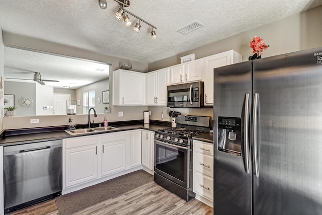 kitchen with a sink, stainless steel appliances, visible vents, dark countertops, and a textured ceiling