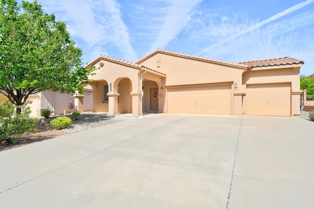 mediterranean / spanish-style house featuring an attached garage, driveway, stucco siding, and a tiled roof