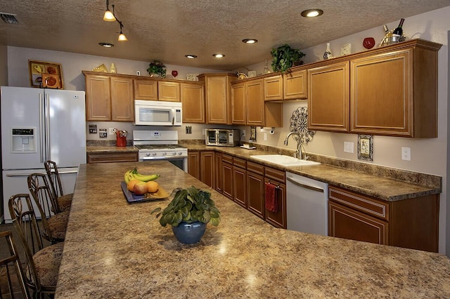 kitchen featuring a textured ceiling, a sink, a breakfast bar, a toaster, and white appliances
