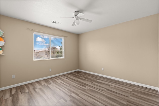 spare room with baseboards, visible vents, wood finished floors, and ceiling fan