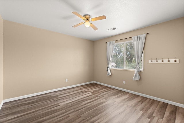 spare room with wood finished floors, a ceiling fan, visible vents, and baseboards