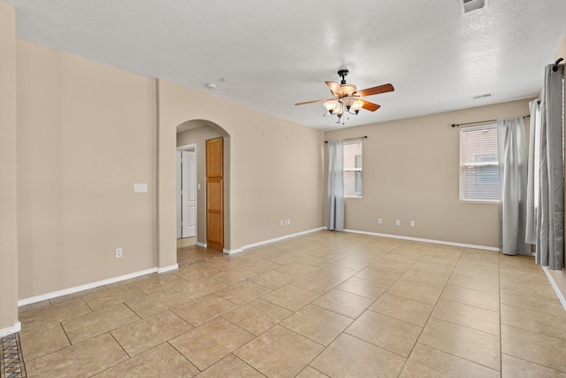 empty room with visible vents, arched walkways, a ceiling fan, and light tile patterned flooring