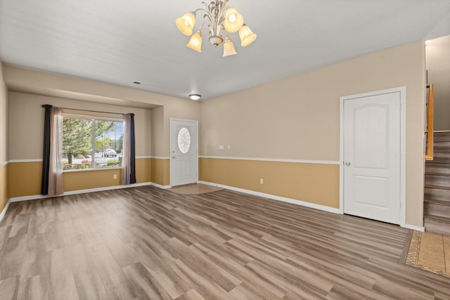 unfurnished living room featuring baseboards, stairway, wood finished floors, and a notable chandelier