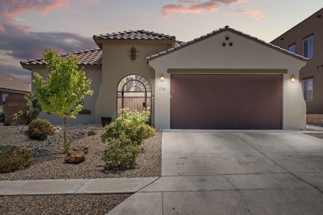 mediterranean / spanish-style house with driveway, an attached garage, a tiled roof, and stucco siding