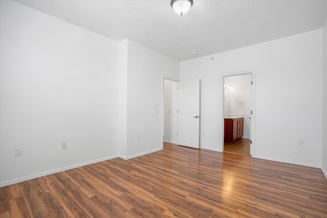 unfurnished bedroom with dark wood finished floors, baseboards, and ensuite bath