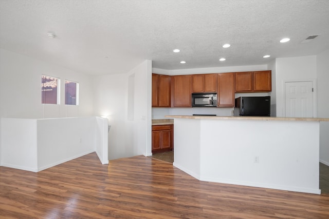 kitchen featuring dark wood finished floors, recessed lighting, freestanding refrigerator, brown cabinetry, and a textured ceiling