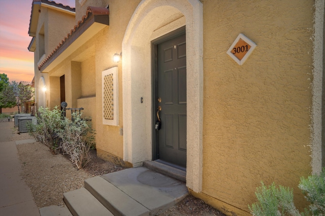 exterior entry at dusk featuring central AC, stucco siding, and a tiled roof