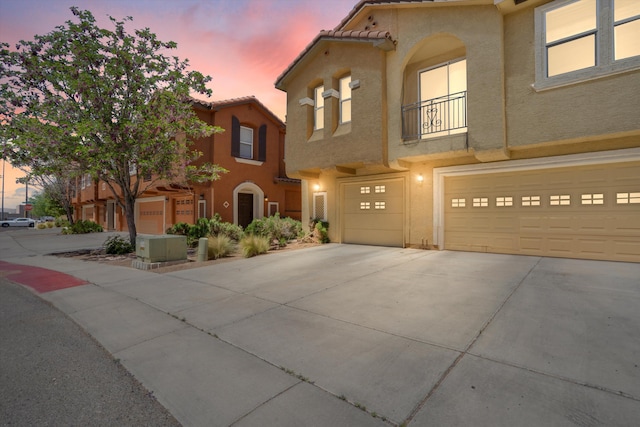 mediterranean / spanish-style home featuring driveway, a balcony, a tile roof, an attached garage, and stucco siding