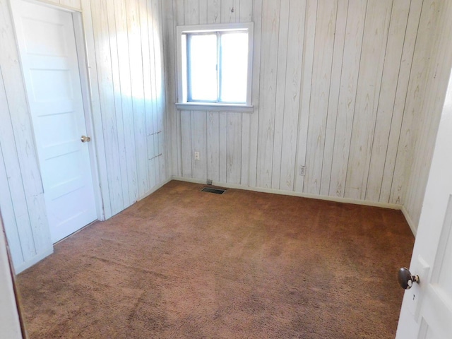 carpeted empty room with wooden walls and visible vents