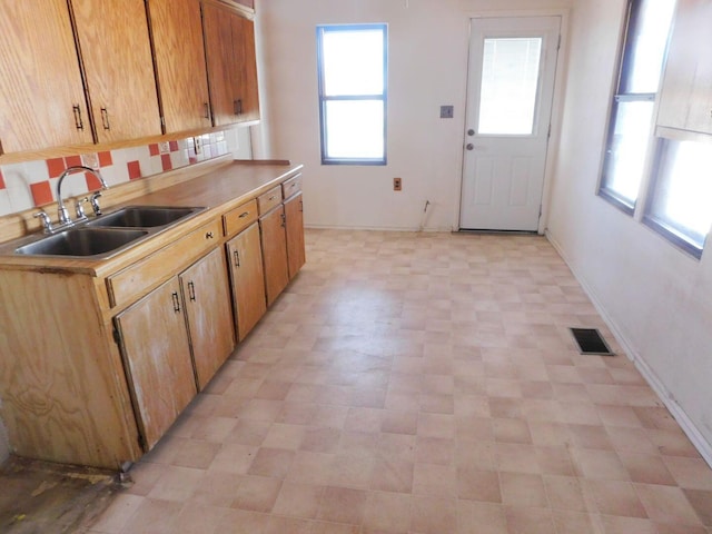 kitchen with baseboards, backsplash, visible vents, and a sink