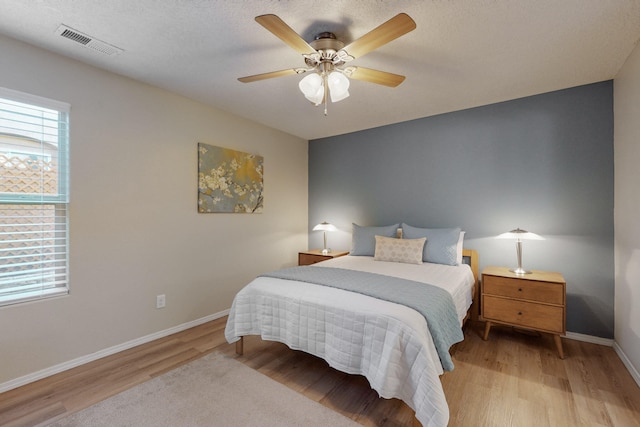 bedroom with a ceiling fan, baseboards, visible vents, and wood finished floors