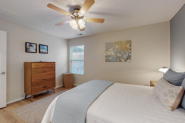 bedroom with baseboards, a ceiling fan, wood finished floors, and visible vents