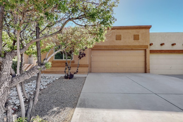 adobe home with an attached garage, stucco siding, and driveway