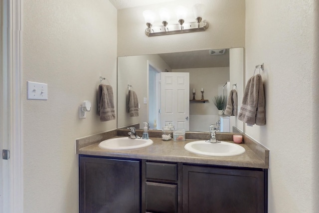 full bath with a textured wall, double vanity, and a sink