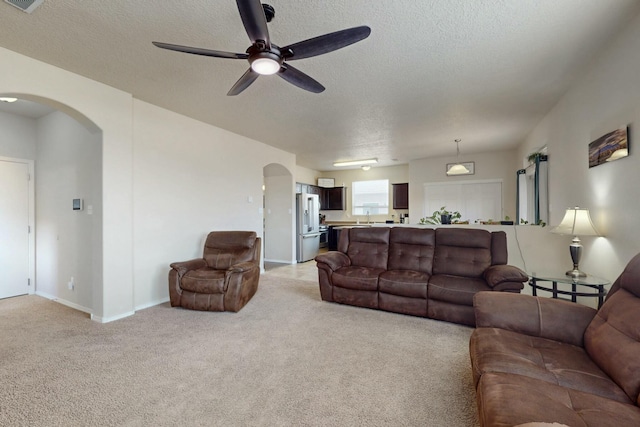 living room featuring arched walkways, ceiling fan, a textured ceiling, and light carpet