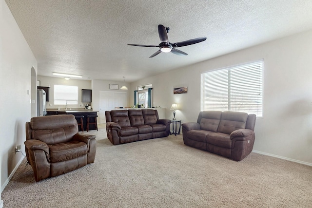 living area featuring a textured ceiling, light colored carpet, baseboards, arched walkways, and a ceiling fan