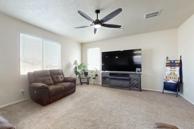 carpeted living area featuring a wealth of natural light, visible vents, a ceiling fan, and a textured ceiling