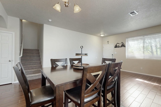 dining space featuring stairway, visible vents, baseboards, a textured ceiling, and wood finished floors