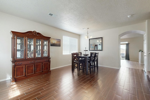dining space featuring arched walkways, a wealth of natural light, visible vents, a textured ceiling, and dark wood-type flooring