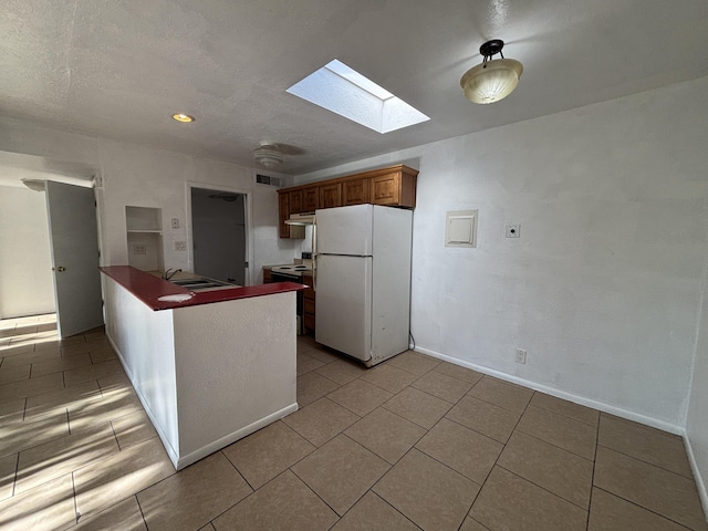 kitchen featuring light tile patterned floors, a skylight, a peninsula, and freestanding refrigerator