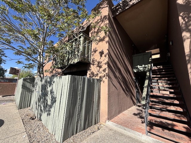 view of side of property with fence, stairway, and stucco siding