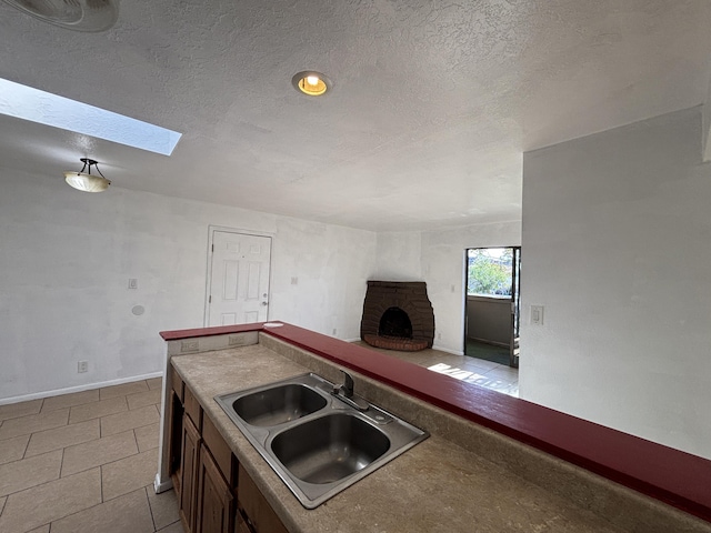 kitchen with a skylight, a fireplace, a sink, baseboards, and a textured ceiling