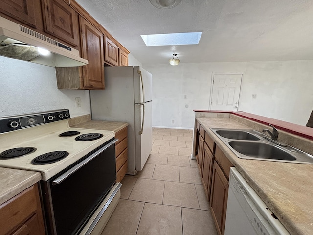 kitchen featuring a skylight, white appliances, light tile patterned floors, under cabinet range hood, and a sink