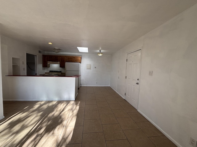 kitchen featuring range with electric cooktop, freestanding refrigerator, under cabinet range hood, tile patterned flooring, and a skylight