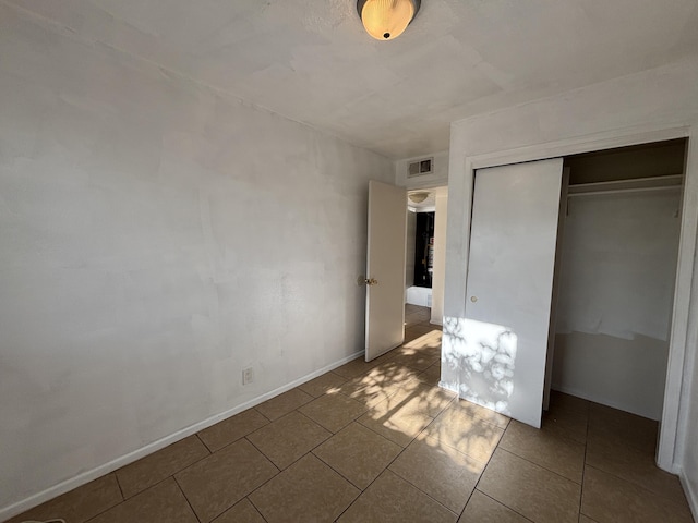 unfurnished bedroom featuring tile patterned floors, visible vents, baseboards, and a closet