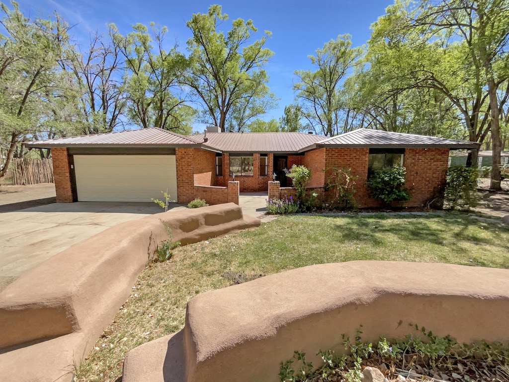 single story home featuring concrete driveway, metal roof, a front yard, an attached garage, and brick siding