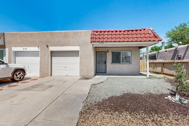 view of front of home featuring fence, an attached garage, a tile roof, stucco siding, and concrete driveway