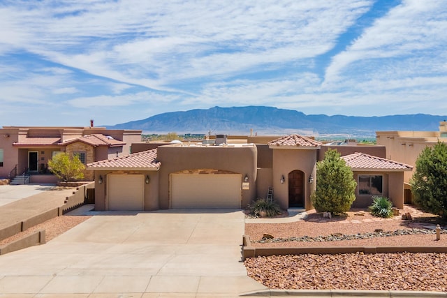 pueblo-style home with stucco siding, a tiled roof, a garage, a mountain view, and concrete driveway