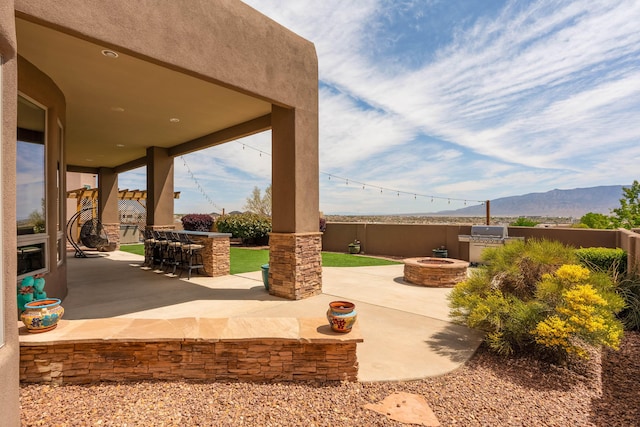 view of patio / terrace with a fenced backyard, exterior kitchen, outdoor dry bar, a mountain view, and a fire pit