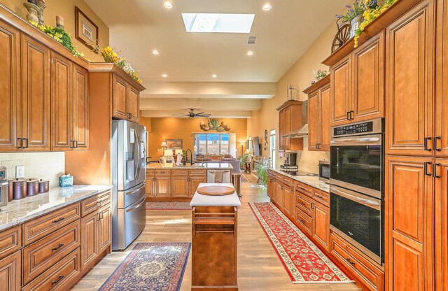3919 Bryan Ave NW, Albuquerque, NM 87114 - kitchen with stainless steel appliances, brown cabinetry, light wood-style flooring, a skylight, and recessed lighting