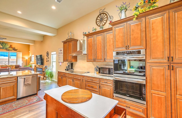 3919 Bryan Ave NW, Albuquerque, NM 87114 - kitchen featuring stainless steel appliances, wall chimney range hood, brown cabinetry, light wood-type flooring, and open floor plan