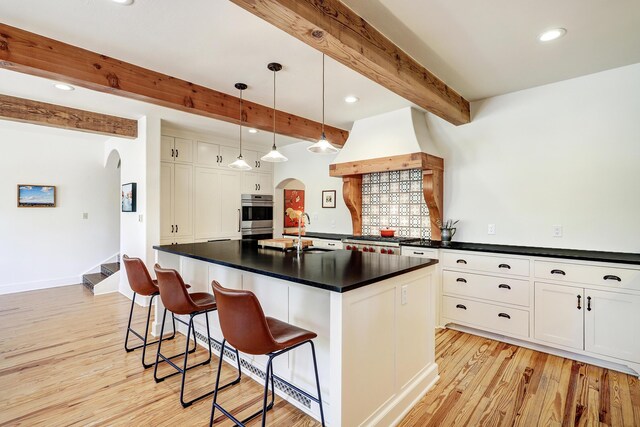 107 Rome Ln, Corrales, NM 87048 - kitchen with arched walkways, custom range hood, beam ceiling, light wood-style flooring, and stainless steel double oven