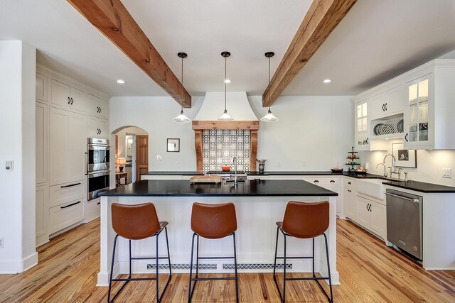 107 Rome Ln, Corrales, NM 87048 - kitchen featuring appliances with stainless steel finishes, arched walkways, beam ceiling, light wood-style flooring, and a kitchen breakfast bar